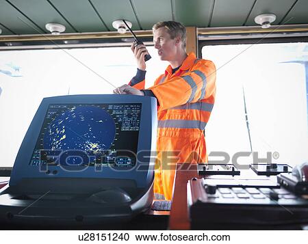 Stock Image - Ship's worker on bridge using walkie-talkie. Fotosearch