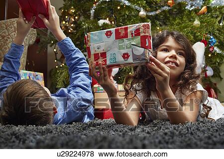 Sister and brother lying in sitting room holding up christmas gifts View Large Photo Image Stock Photo - Sister and brother lying in sitting room holding up christmas gifts. Fotosearch