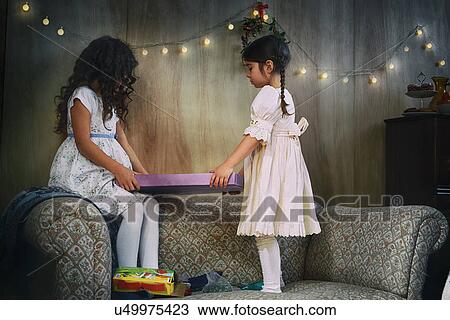 Sisters standing on sitting room sofa handing christmas gift View Large Photo Image Stock Image - Sisters standing on sitting room sofa handing christmas gift. Fotosearch