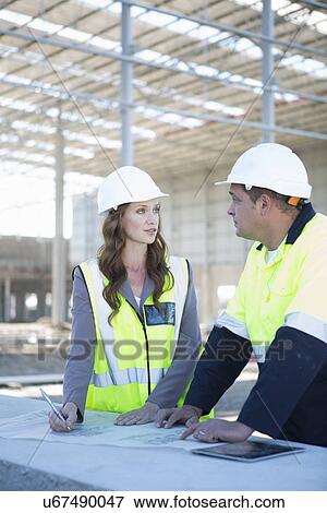 Stock Photo - Site manager and architect with digital tablet and blueprint on construction site. Fotosearch
