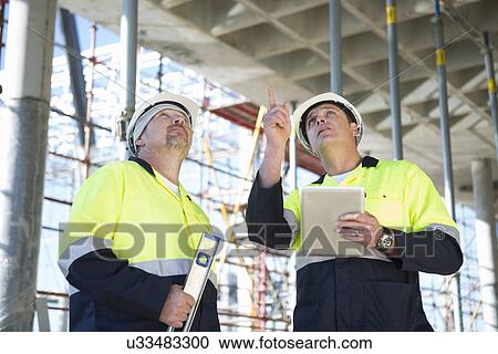 Stock Image - Site manager and builder looking up on construction site. Fotosearch