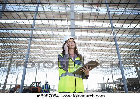 Site manager with clipboard chatting on smartphone on construction site View Large Photo Image Picture - Site manager with clipboard chatting on smartphone on construction site. Fotosearch