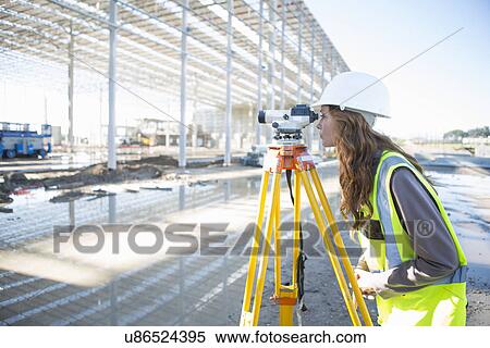 Stock Photography - Surveyor leaning forward to look through level on construction site. Fotosearch