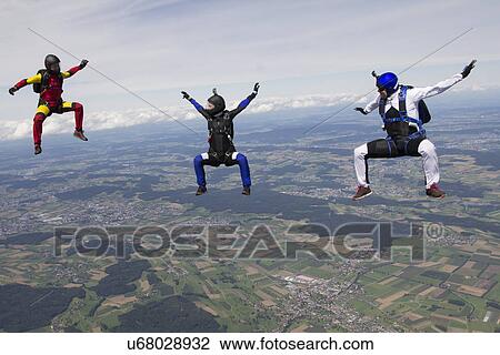 Stock Image - Team of three skydivers in sit fly position over Buttwil, Luzern, Switzerland. Fotosearch