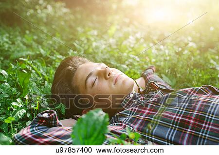 Stock Image - Teenage boy lying in field sleeping. Fotosearch