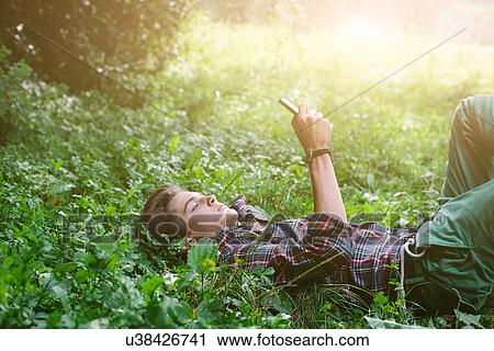 Stock Image - Teenage boy lying in field using cell phone. Fotosearch