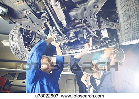 Stock Photo - Three college students looking up at car in garage workshop. Fotosearch