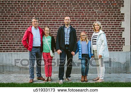 Stock Image - Three generation family standing by brick wall. Fotosearch