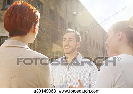 Stock Image - Three young people talking, building in background. Fotosearch