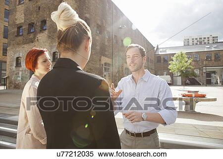 Stock Photography - Three young people talking, building in background, East London, UK. Fotosearch