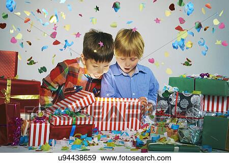 Stock Photo - Two brothers open mouthed on unwrapping glowing christmas gift box with exploding confetti. Fotosearch