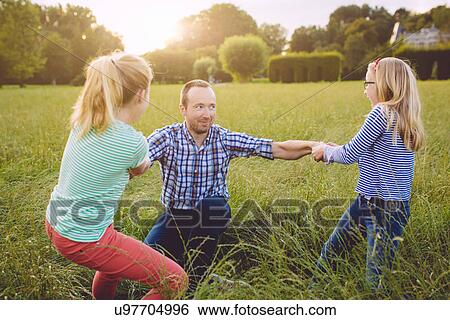 Stock Photograph - Two girls pulling father up off ground. Fotosearch