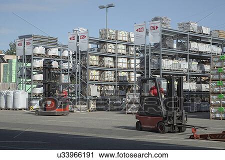 Stock Image - Two male warehouse workers moving stock in fork lift trucks. Fotosearch