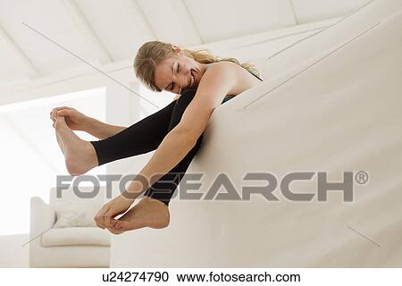 Stock Image - Woman dangling legs over sofa. Fotosearch