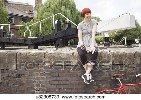 Woman listening to music by canal, East London, UK View Large Photo Image Stock Photo - Woman listening to music by canal, East London, UK. Fotosearch