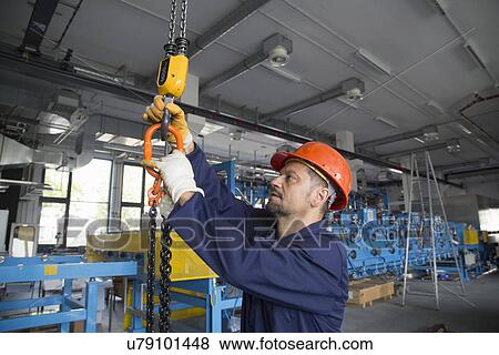 Stock Photo - Worker adjusting chain hoist in industrial plant. Fotosearch