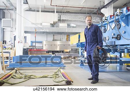 Worker carrying reel of cable in industrial plant View Large Photo Image Picture - Worker carrying reel of cable in industrial plant. Fotosearch