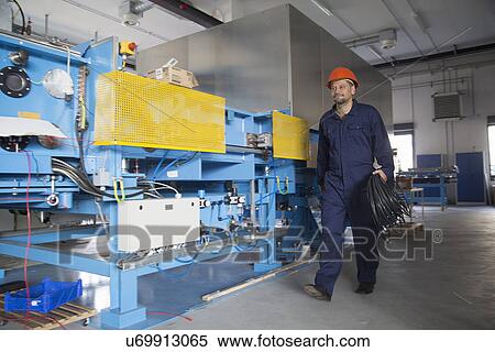 Stock Photography - Worker carrying reel of cable in industrial plant. Fotosearch