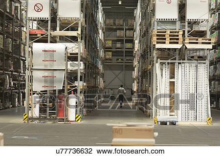 Stock Image - Worker searching for stock in aisles of hardware store warehouse. Fotosearch