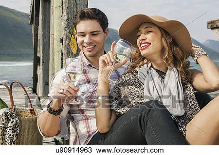 Stock Image - Young couple drinking wine on old pier, Cape Town, Western Cape, South Africa. Fotosearch
