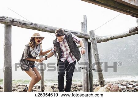 Stock Photo - Young couple ducking under old pier, Cape Town, Western Cape, South Africa. Fotosearch