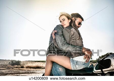 Stock Photo - Young couple hugging and straddling motorcycle on arid plain, Cagliari, Sardinia, Italy. Fotosearch