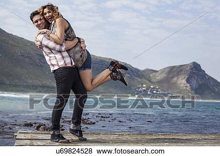 Stock Photo - Young couple hugging on coastal pier, Cape Town, Western Cape, South Africa. Fotosearch