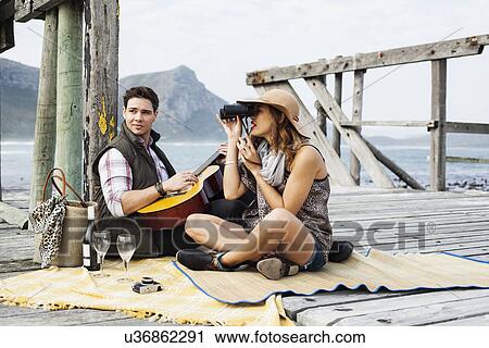 Stock Image - Young couple picnicing on old pier, Cape Town, Western Cape, South Africa. Fotosearch