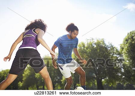 Stock Image - Young couple playing soccer in park. Fotosearch
