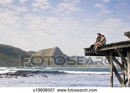 Stock Photo - Young couple sitting on edge of old pier, Cape Town, Western Cape, South Africa. Fotosearch