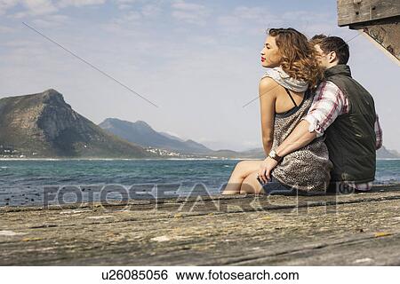 Stock Photograph - Young couple sitting on edge of pier, Cape Town, Western Cape, South Africa. Fotosearch