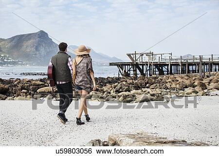 Young couple strolling on beach carrying guitar, Cape Town, Western Cape, South Africa View Large Photo Image Stock Photograph - Young couple strolling on beach carrying guitar, Cape Town, Western Cape, South Africa. Fotosearch
