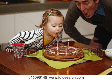 Stock Photography - Young girl blowing out birthday candles on cake. Fotosearch