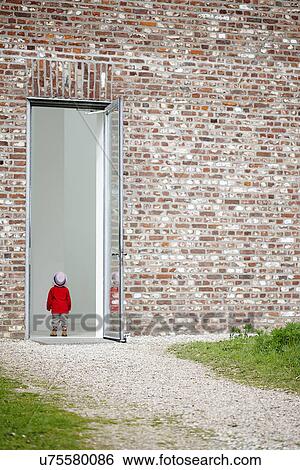Stock Photograph - Young girl standing in doorway in brick wall. Fotosearch