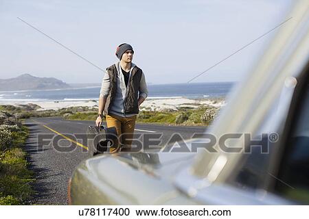 Stock Image - Young man behind parked car with guitar case, Cape Town, Western Cape, South Africa. Fotosearch