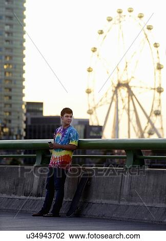 Stock Image - Young man holding mobile phone, skateboard beside him. Fotosearch