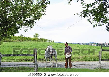 Young man in cowboy gear leading horse through gateway View Large Photo Image Stock Image - Young man in cowboy gear leading horse through gateway. Fotosearch
