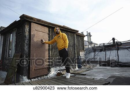 Stock Image - Young man leaning against rooftop hut and looking away. Fotosearch