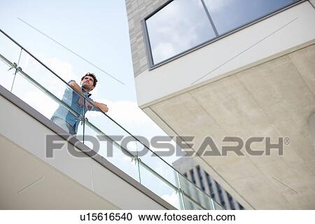 Stock Image - Young man leaning on balcony, low angle. Fotosearch