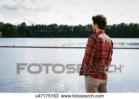 Stock Image - Young man looking across water. Fotosearch