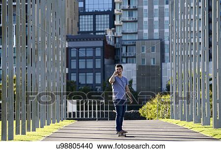 Stock Image - Young man on skateboard, using mobile phone. Fotosearch