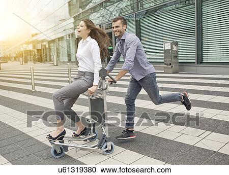Young man pushing woman on luggage trolley View Large Photo Image Stock Image - Young man pushing woman on luggage trolley. Fotosearch