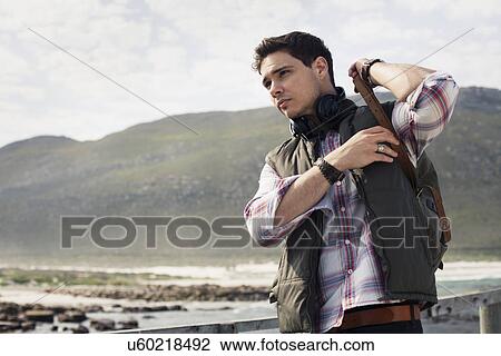 Stock Image - Young man putting on rucksack, Cape Town, Western Cape, South Africa. Fotosearch