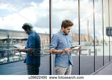 Young man reading newspaper by glass window View Large Photo Image Stock Photography - Young man reading newspaper by glass window. Fotosearch