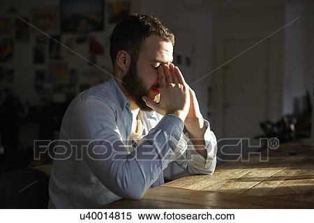 Young man sitting at kitchen table with hands on face View Large Photo Image Stock Photography - Young man sitting at kitchen table with hands on face. Fotosearch