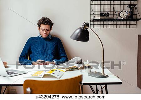 Young man using cell phone at desk View Large Photo Image Stock Photo - Young man using cell phone at desk. Fotosearch