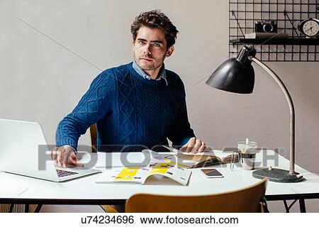 Stock Photograph - Young man using laptop at desk. Fotosearch