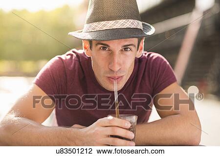 Stock Image - Young man wearing hat drinking through straw. Fotosearch