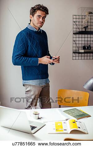 Young man with cell phone by desk, portrait View Large Photo Image Stock Photography - Young man with cell phone by desk, portrait. Fotosearch