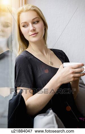 Young woman drinking coffee whilst looking out of window View Large Photo Image Stock Photo - Young woman drinking coffee whilst looking out of window. Fotosearch